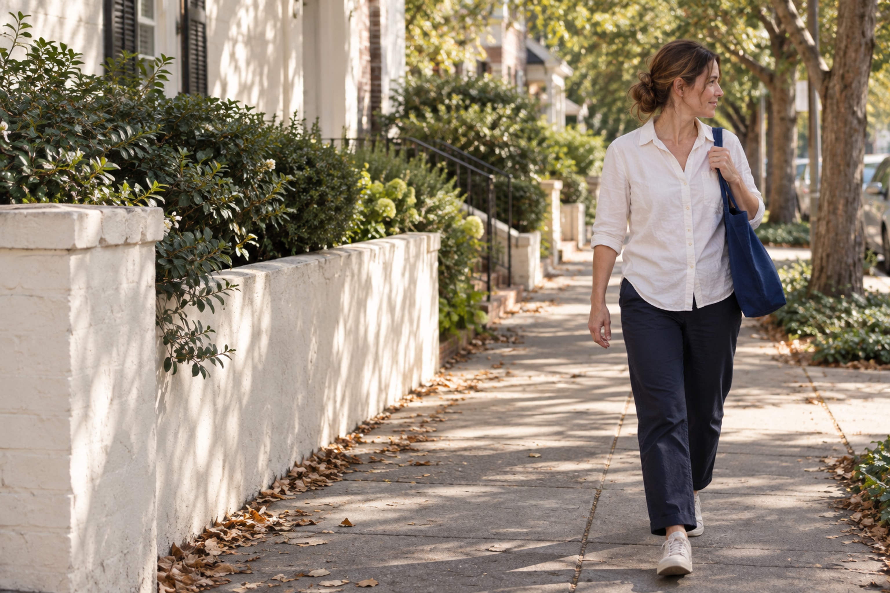 The same woman walking along a neighborhood street with her blue canvas tote.